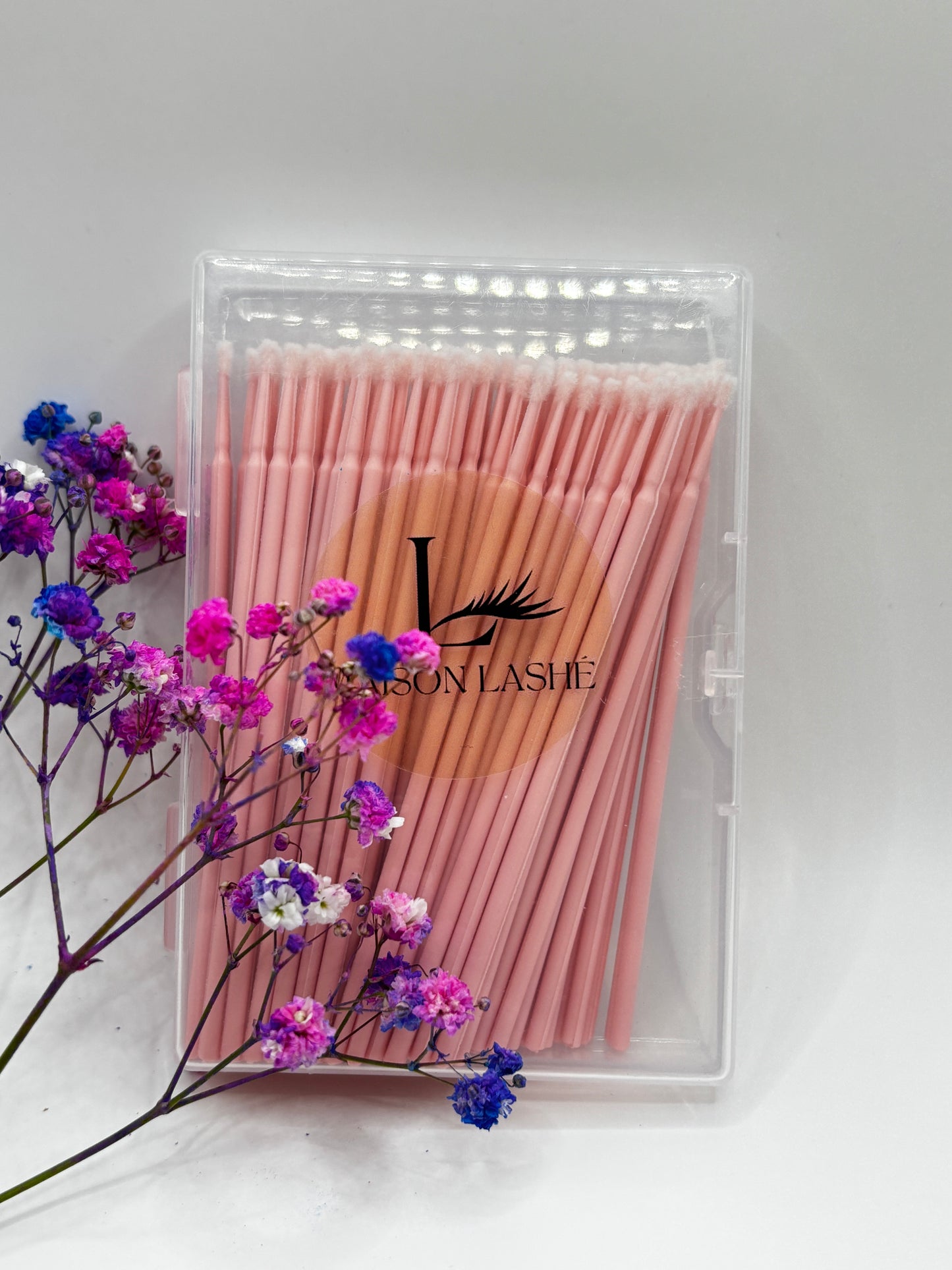 Maison Lashé microfibre brushes 100pcs packaged in a clear case with pink brushes and decorative flowers on a white background